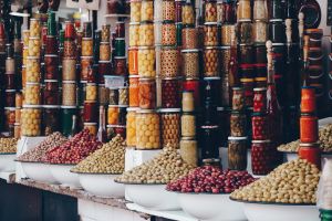 Colorful jars of preserved olives and bowls of different types of olives at a market.