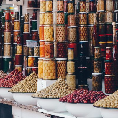 Colorful jars of preserved olives and bowls of different types of olives at a market.