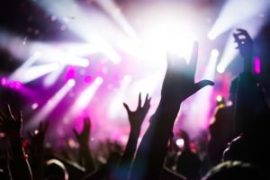 Crowd at a music festival with hands raised and bright stage lights.