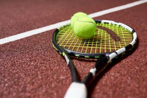 Tennis racquet with two tennis balls on a clay court.