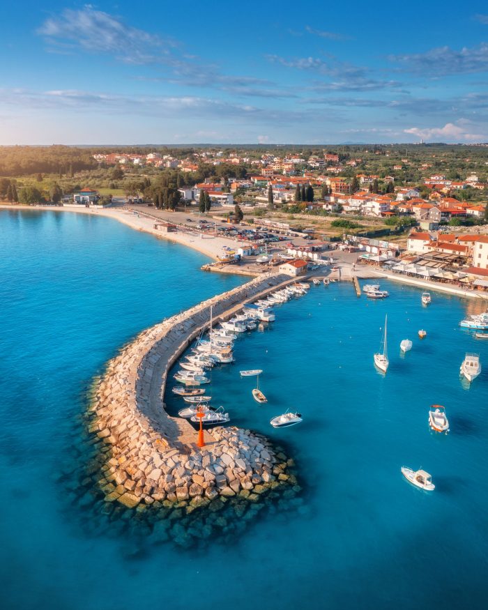 Aerial view of boats and luxury yachts in the dock, breakwater, and old city of Fažana at sunset in Istria, Croatia.