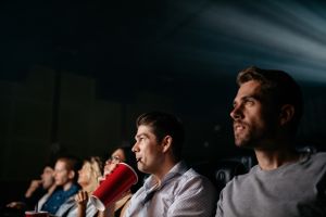 Un jeune homme regarde un film avec des amis dans une salle de cinéma.