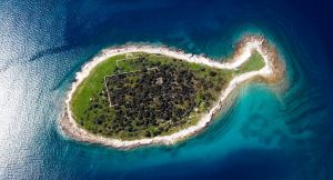 Aerial view of a lush, green island with ancient ruins surrounded by turquoise waters in Brijuni National Park.