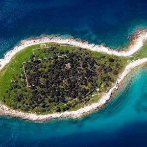 Aerial view of a lush, green island with ancient ruins surrounded by turquoise waters in Brijuni National Park.